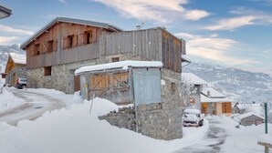 A rustic wooden chalet with stone walls, a snow-covered roof, and a clear sky. - Chalet “Le petit Paradis” in the heart of the 3 valleys! (Les Belleville)