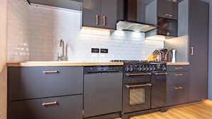 A modern kitchen with dark cabinetry, a white tiled backsplash, a stainless steel range hood, and a built-in oven. - Chalet “Le petit Paradis” in the heart of the 3 valleys! (Les Belleville)