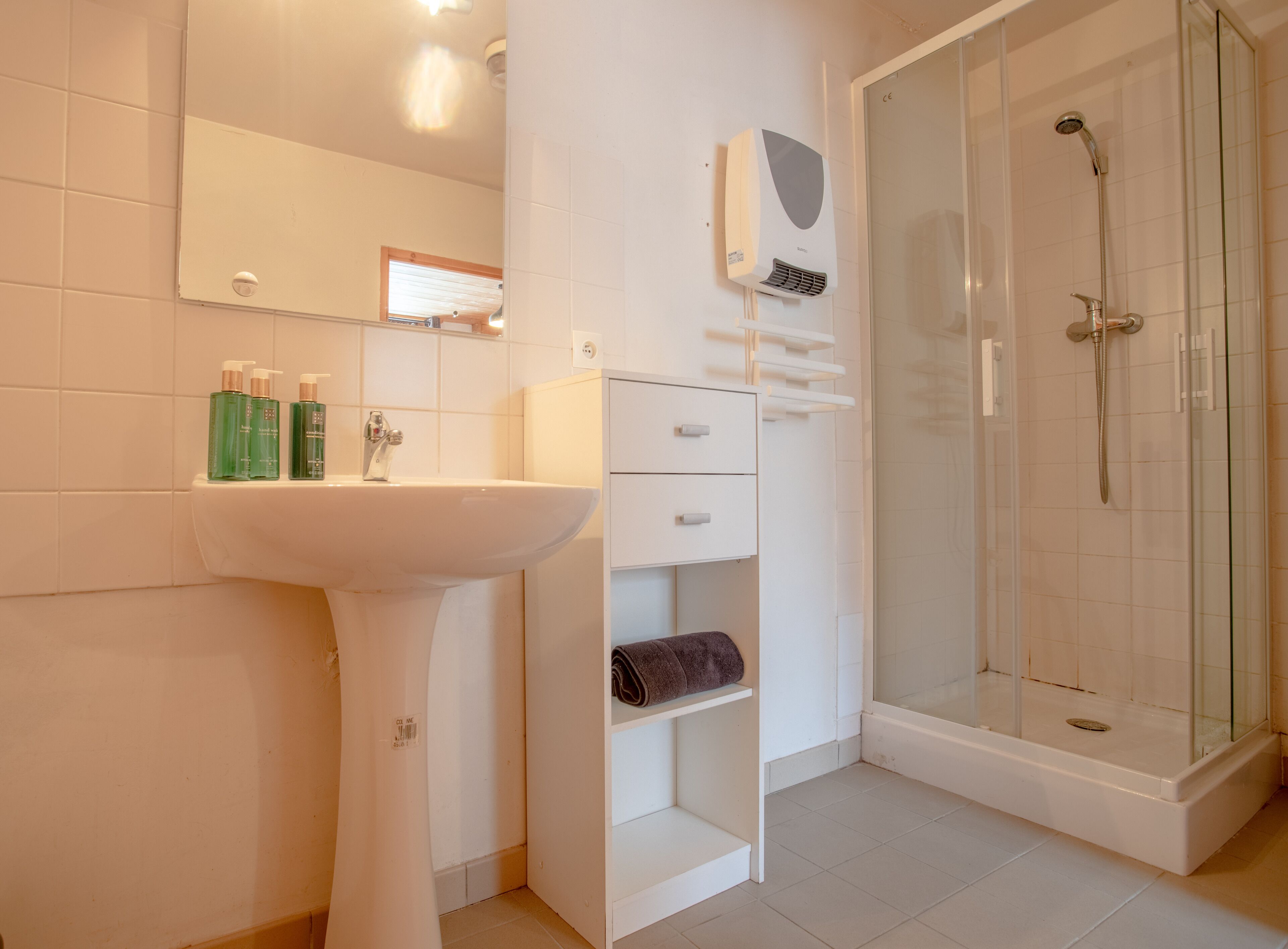 Een badkamer met een wastafel, spiegel, handdoekhouder en een douche met glazen wanden.