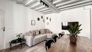 A modern living room with a sectional sofa, a dining table, and a large TV. - Appartement au Coeur de Ville (Sens)