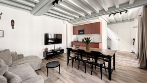 A modern living room with a sofa, TV, and dining area with chairs and a table. - Appartement au Coeur de Ville (Sens)
