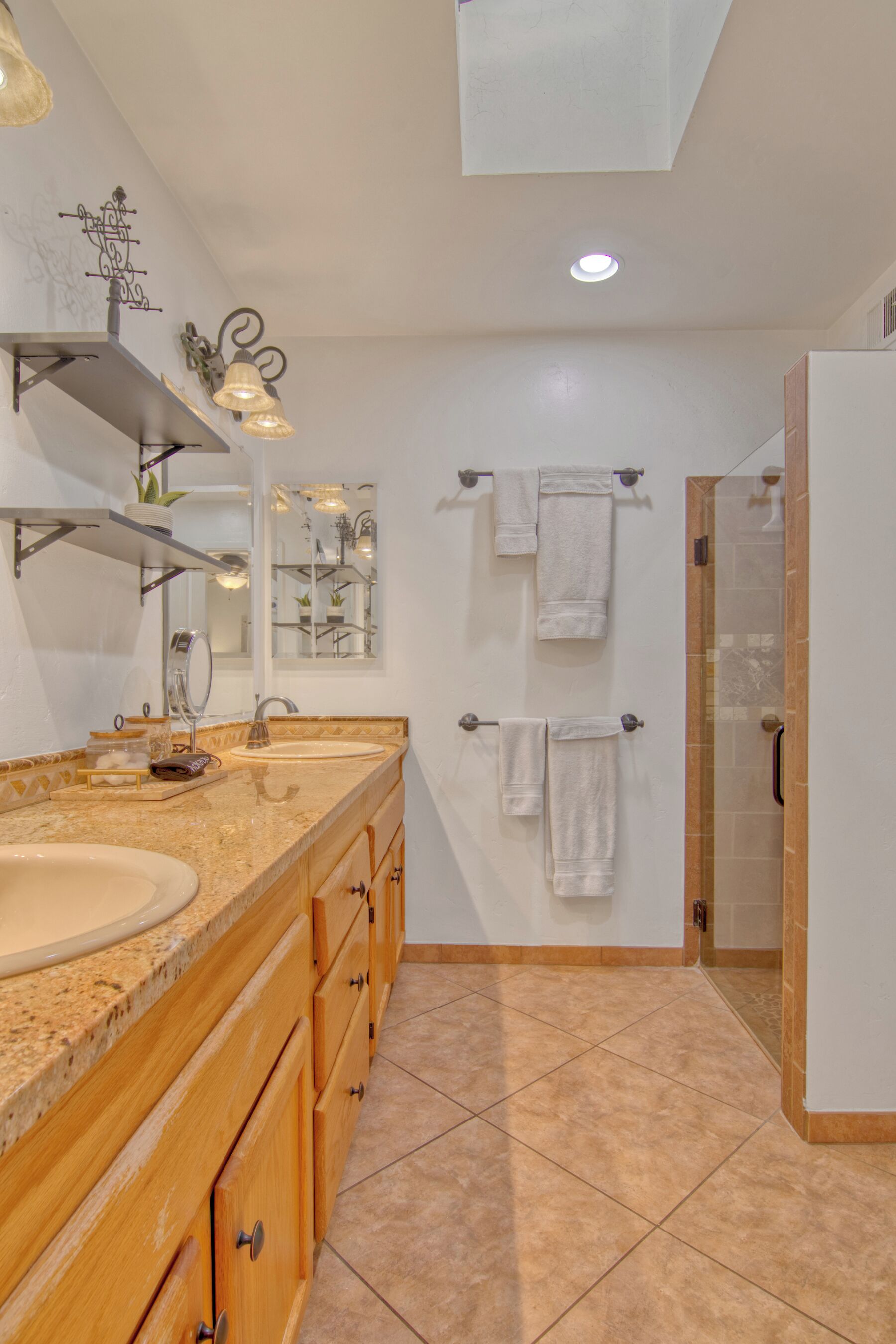 Une salle de bain moderne dotée d’un grand lavabo, d’un meuble-lavabo en bois, de plusieurs porte-serviettes et d’une cabine de douche en verre.