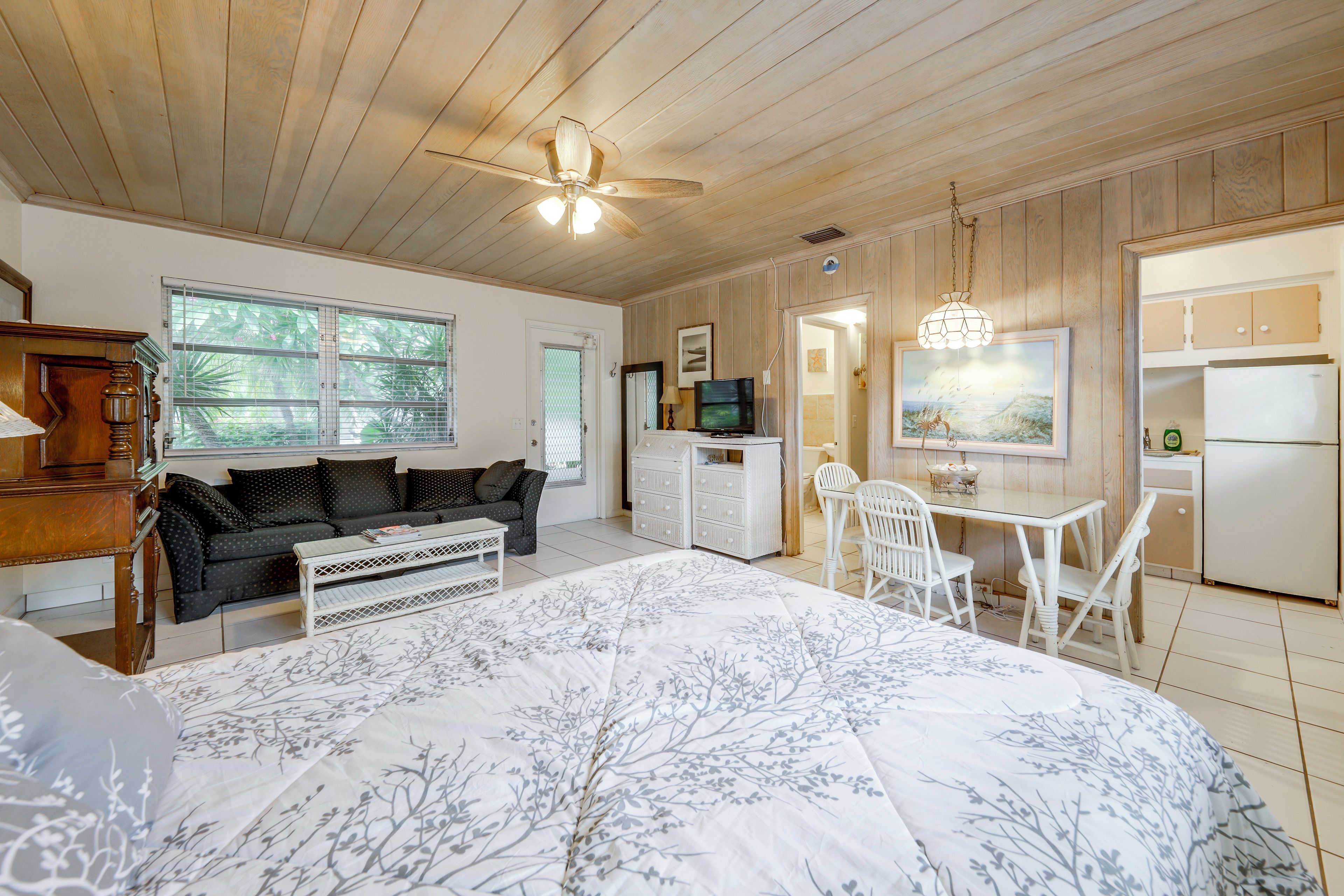 A bedroom with a bed, a desk, a chair, a television, and a kitchenette.