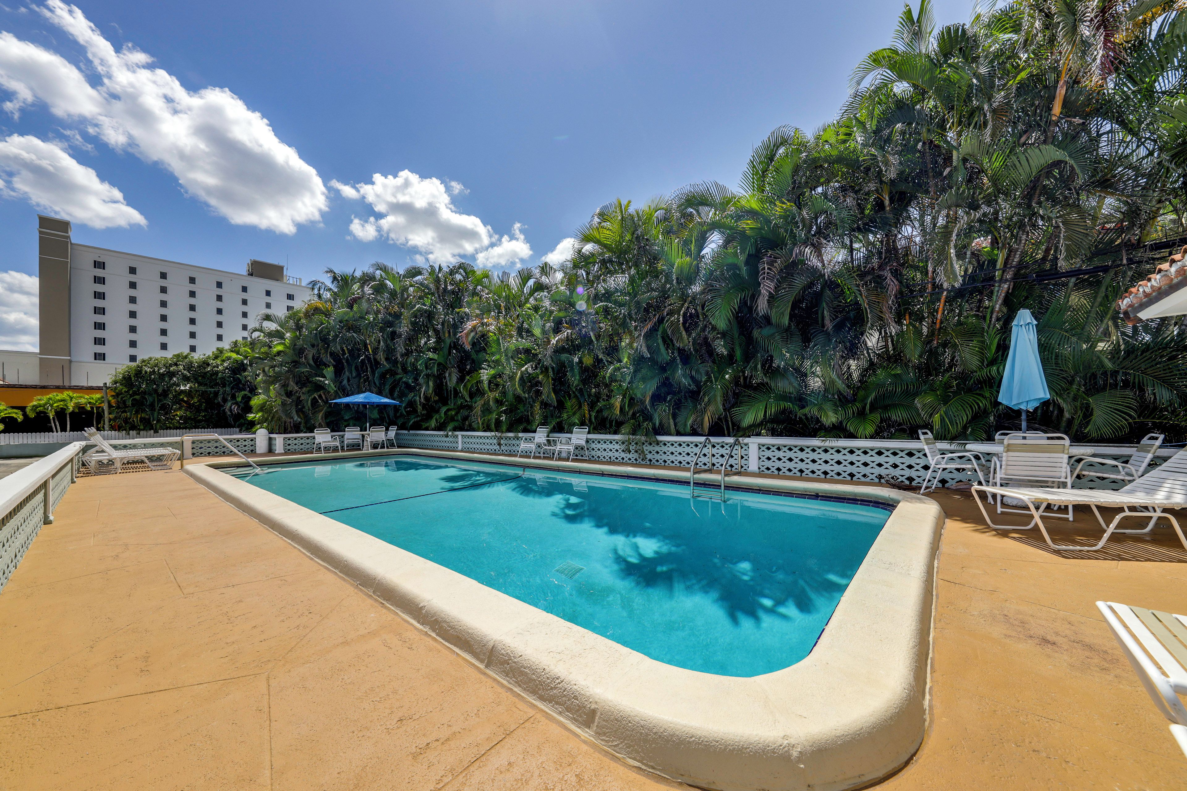 A swimming pool with a white deck, surrounded by palm trees and a white fence.