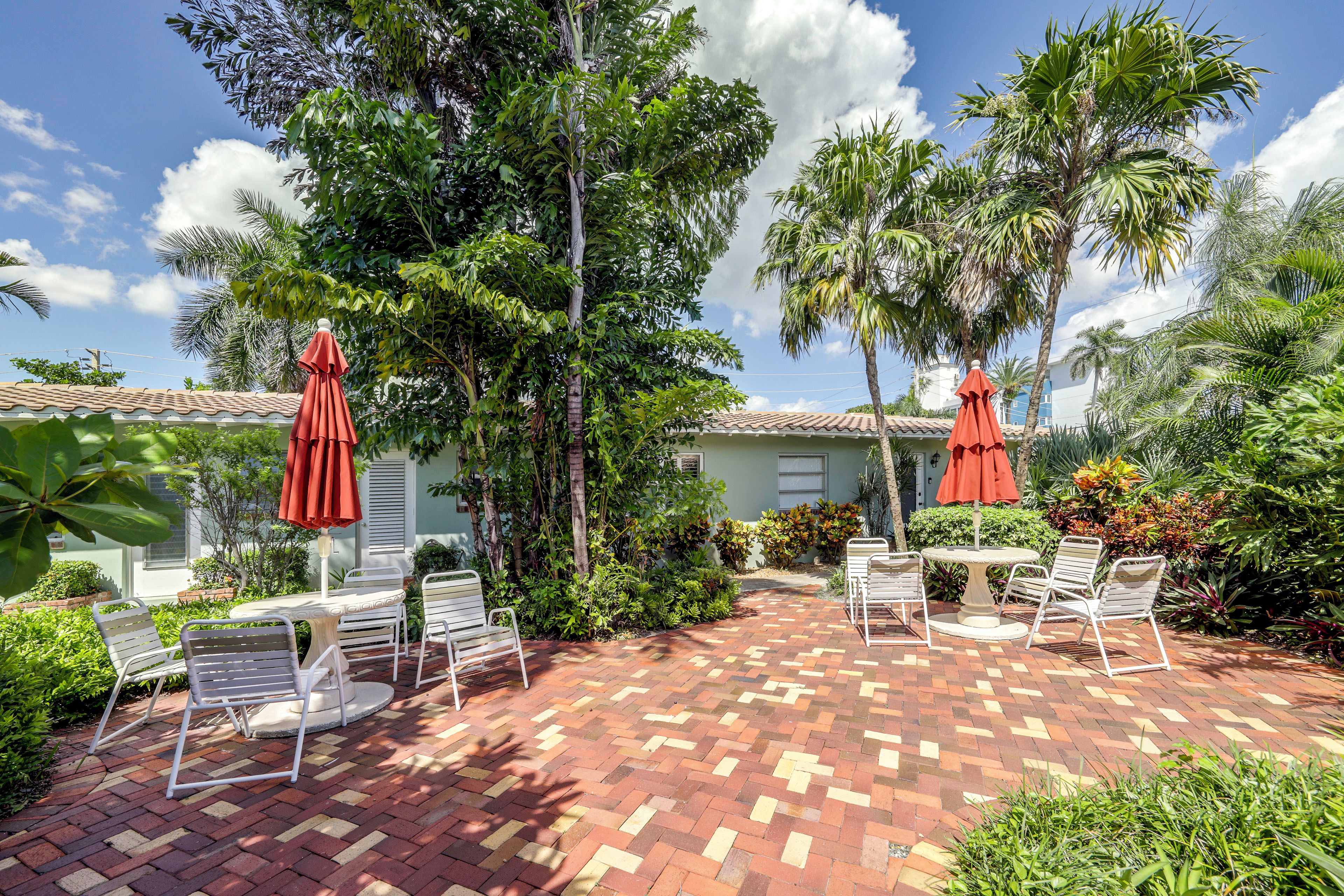A patio with outdoor furniture and umbrellas, surrounded by lush greenery and palm trees.