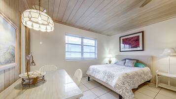 A room with a bed, a table, chairs, a window, and a painting on the wall.