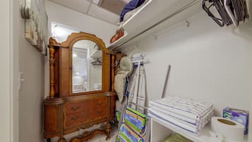 A room with a wooden dresser, a mirror, a hanging rack with clothes, and a shelf with towels.