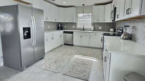 Cocina moderna con armarios blancos, electrodomésticos de acero inoxidable, lavavajillas integrado y una ventana con persianas.
