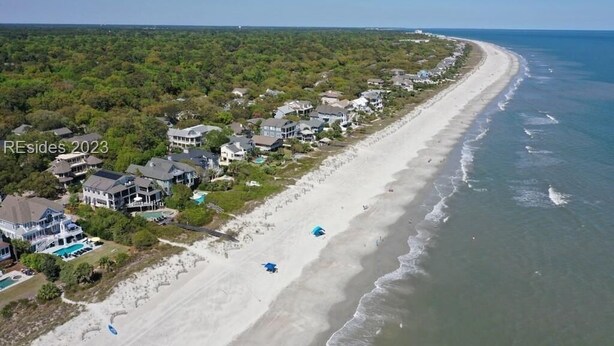 Vista aérea de uma área residencial costeira com casas ao longo de uma praia arenosa e o oceano.