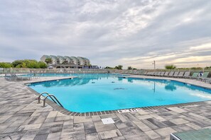 A swimming pool with a tiled deck, a lifeguard stand, and a building with a green roof in the background.