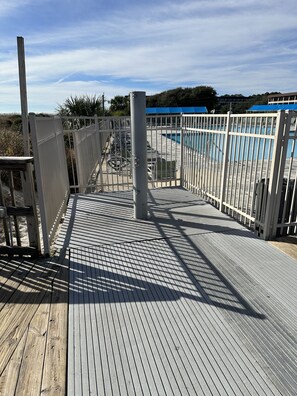 A wooden deck with a metal railing, leading to a pool area with blue umbrellas.