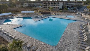 Uma piscina retangular com um deck ladrilhado, rodeada por espreguiçadeiras e guarda-sóis.