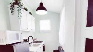 Une cuisine étroite avec des meubles blancs, un four à micro-ondes et un luminaire suspendu noir.