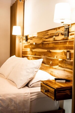 A hotel room with a wooden headboard, a bedside table with a lamp, and a remote control.