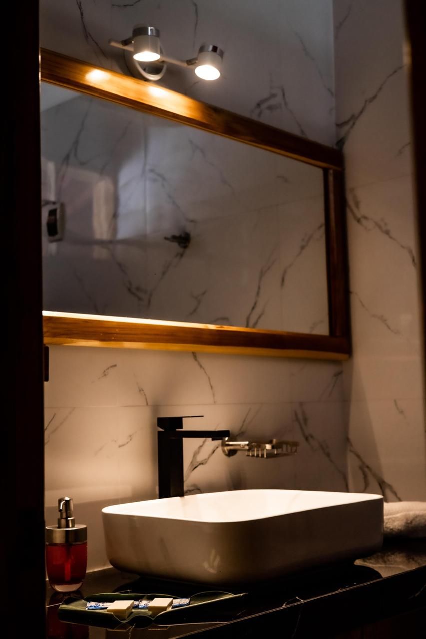 A bathroom with a marble wall, a white sink with a black faucet, and a mirror with a wooden frame.