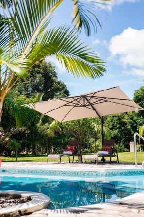 A swimming pool with lounge chairs and a large umbrella.