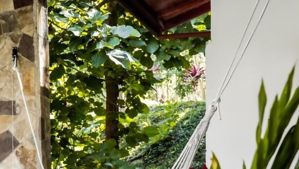 A round glass table with a textured vase, a hammock, and a stone wall.