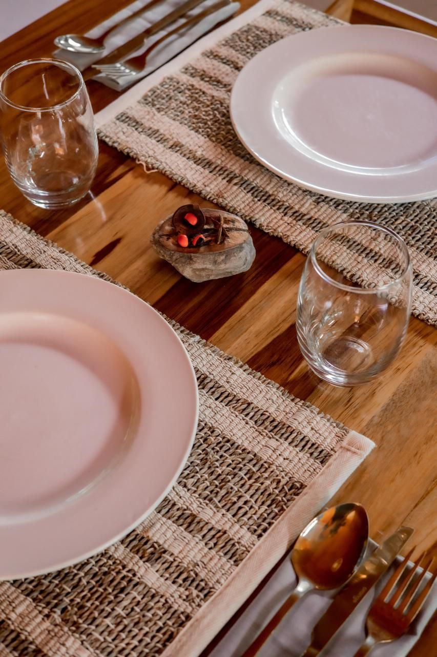 Una mesa puesta con platos, vasos, cubiertos y un posavasos tejido.