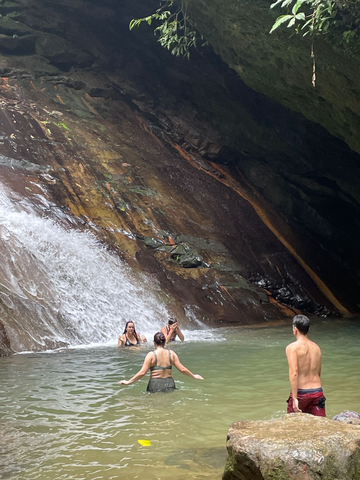 A natural water body with a waterfall, surrounded by rocky terrain and vegetation.