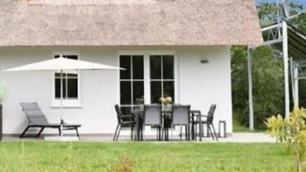 Une maison dotée d’un toit incurvé original, d’un patio avec des meubles d’extérieur et d’un ciel dégagé.