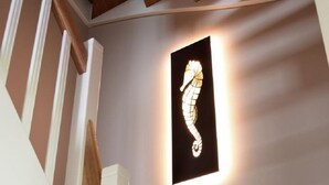 Un escalier avec des rampes en bois et un luminaire mural orné d’un motif représentant un hippocampe.