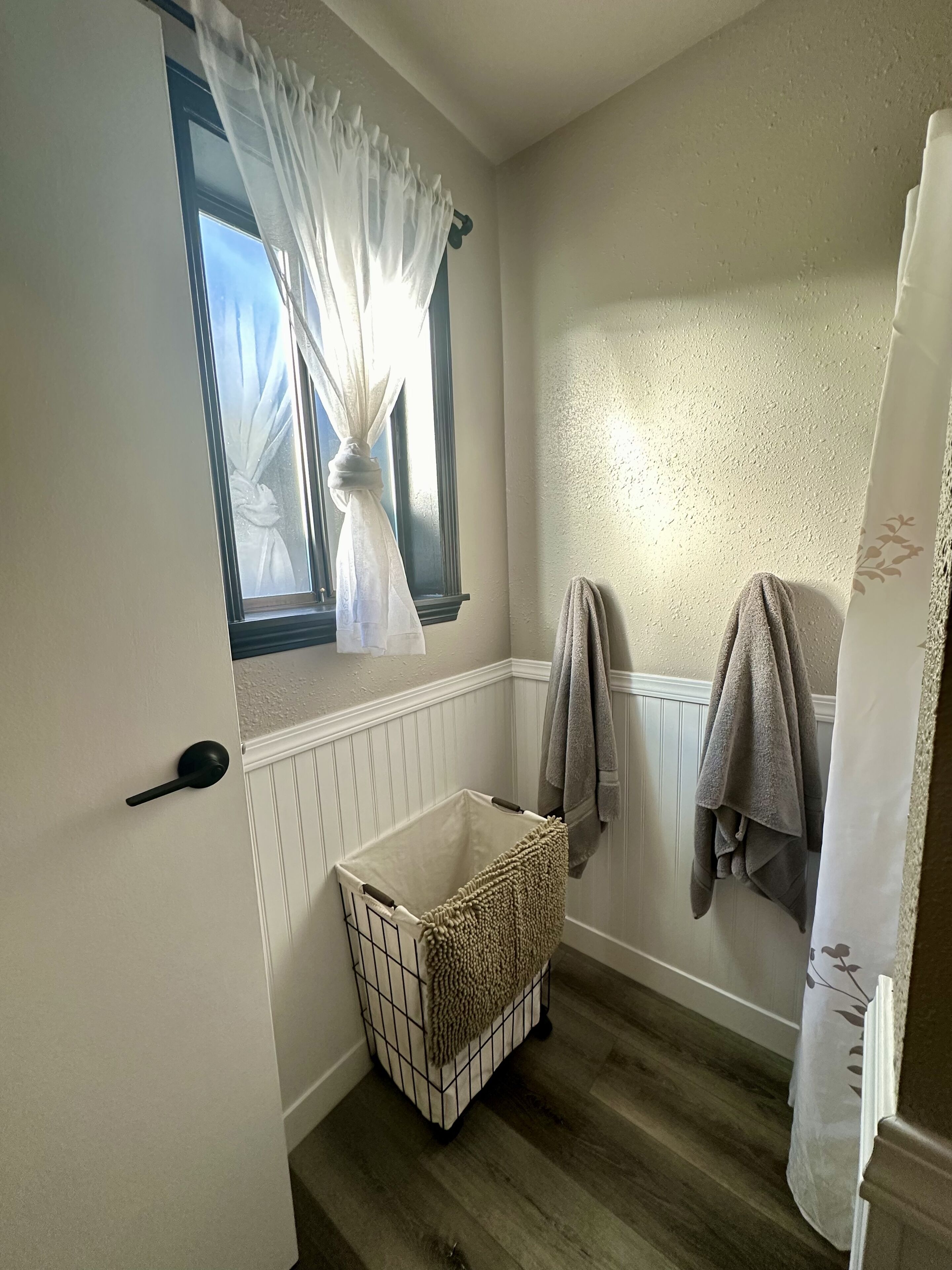 Ein Badezimmer mit Fenster, Wäschekorb und Handtüchern, die an der Wand hängen.