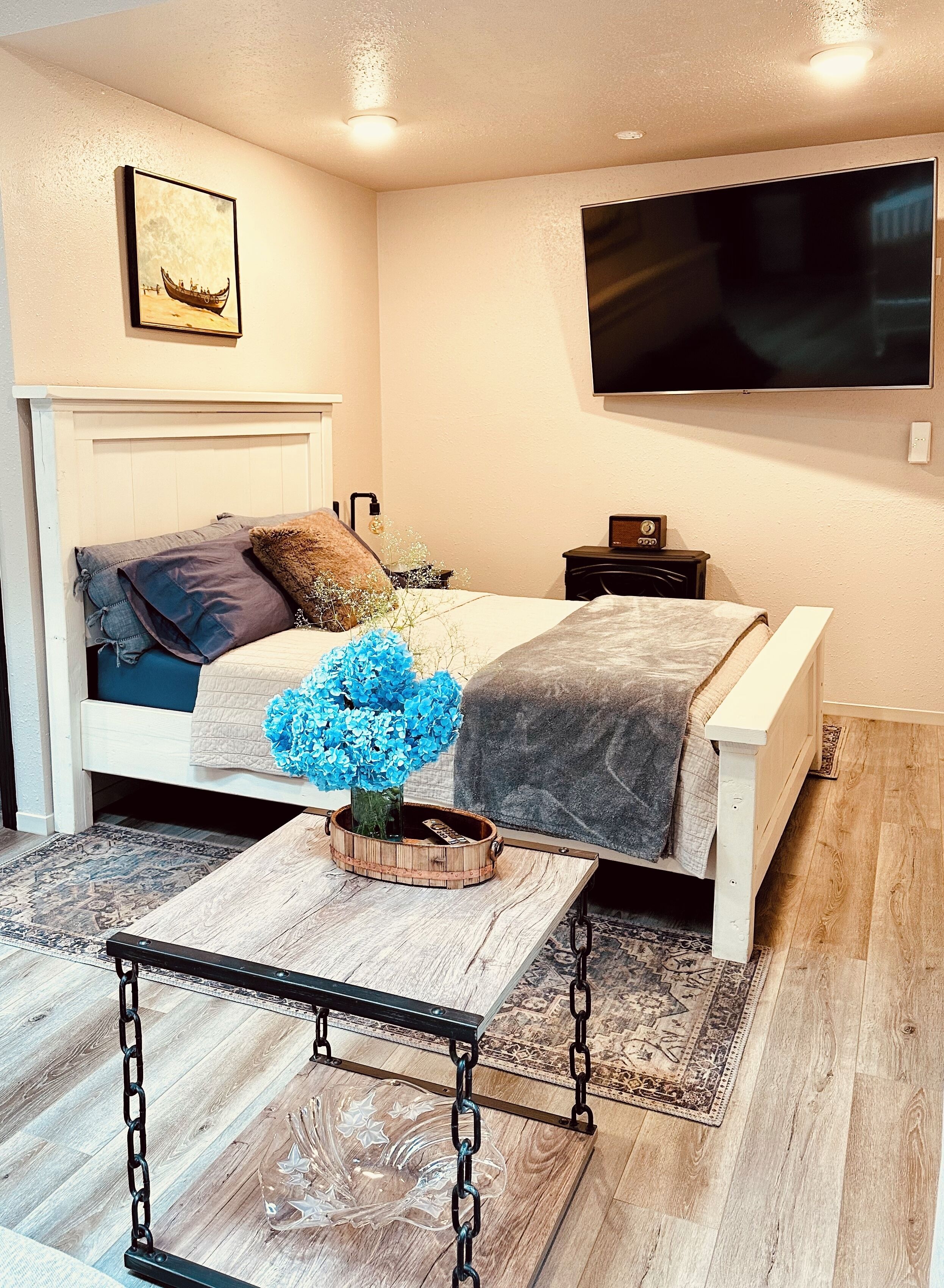 A bedroom with a bed, a TV mounted on the wall, and a wooden coffee table with a vase of flowers.