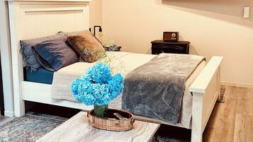 A bedroom with a bed, a TV mounted on the wall, and a wooden coffee table with a vase of flowers.