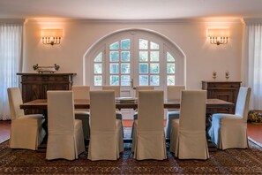 Uma sala de jantar com uma grande janela em arco, uma mesa de madeira e seis cadeiras.