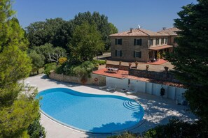Uma villa com piscina, rodeada por vegetação exuberante e um espaço de estar ao ar livre com mesas e cadeiras.