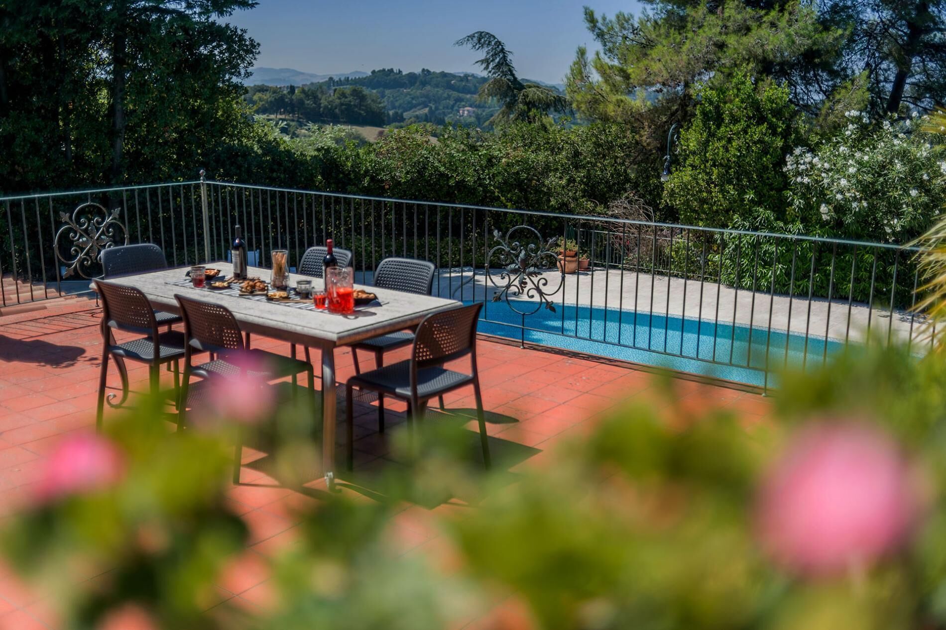 A patio with a table set for dining, a swimming pool, and surrounding greenery.