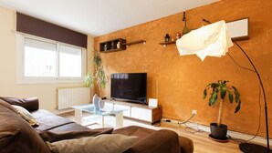 Ein Wohnzimmer mit einer Couch, einem Glastisch, einem Fernseher und einer Topfpflanze.
