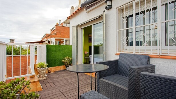 Eine Terrasse mit Korbmöbeln, einem kleinen Tisch und einer Glastür, die zu einem Raum führt.