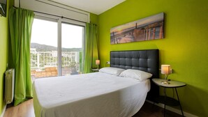 Ein Hotelzimmer mit einem großen Bett, grünen Vorhängen, einem Gemälde an der Wand und Blick auf die Stadt durch das Fenster.