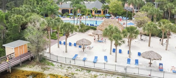 A resort with a pool, lounge chairs, palm trees, and a beach area.