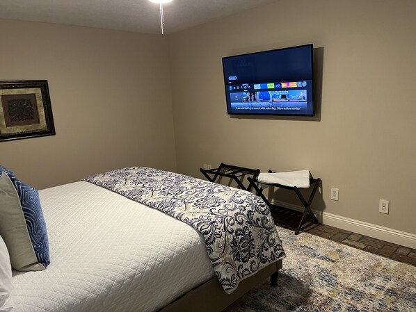Een slaapkamer met een bed, een aan de muur bevestigde televisie en een kleine tafel met een stoel.