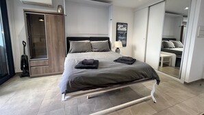 A modern bedroom with a bed, bedside table, lamp, and a large mirror.