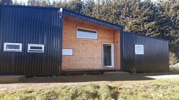 Ein modernes Gebäude mit Holzfassade und Metallverkleidung, mit einer großen Tür und Fenstern.