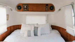 A cozy bed with white bedding and patterned pillows in a well-lit RV interior.