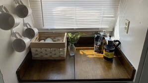 A compact kitchenette with a window, a wooden crate with mugs, a coffee maker, and a plant.