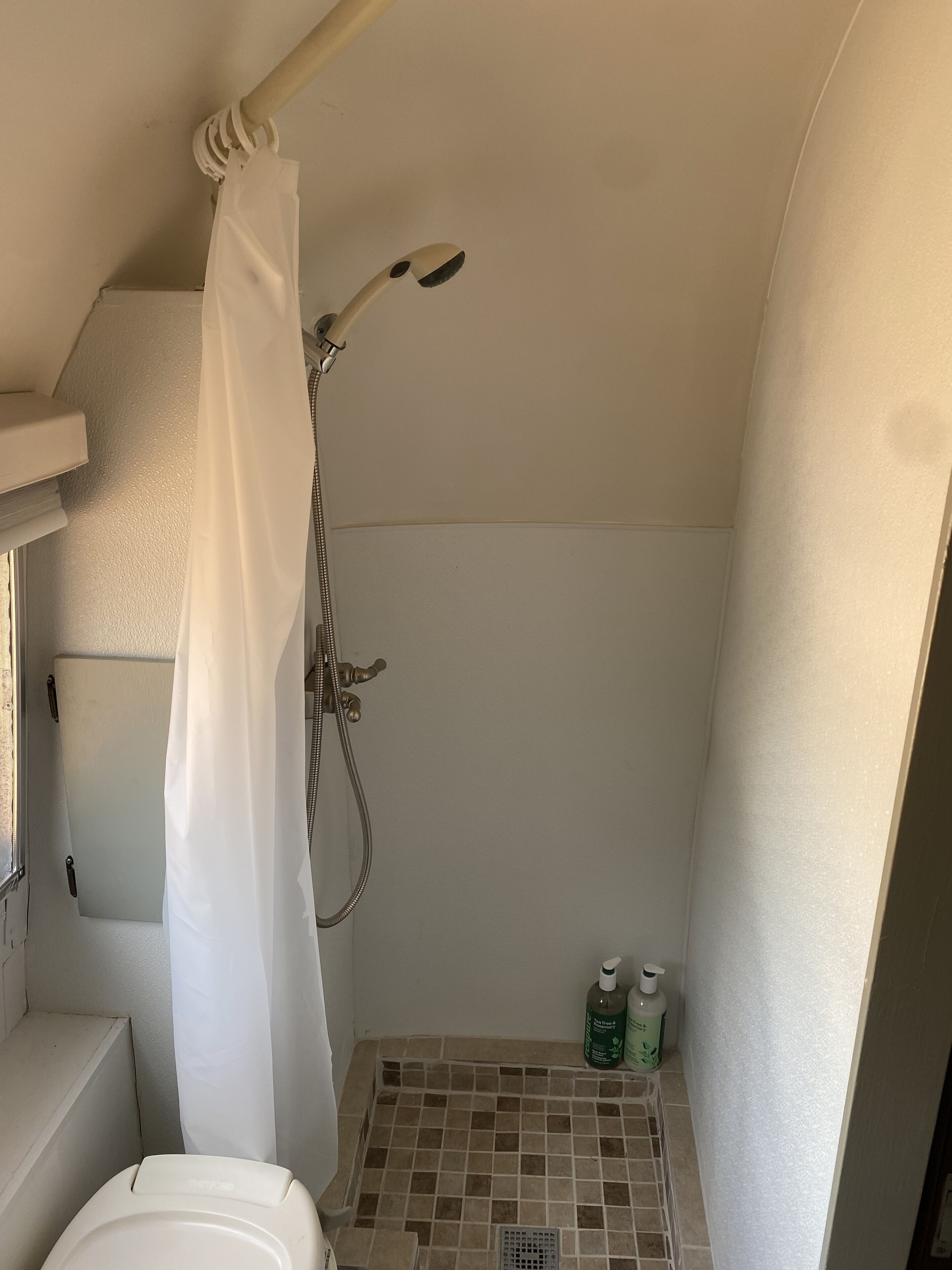 A small, compact shower area with a showerhead, a curtain, and a tiled floor.