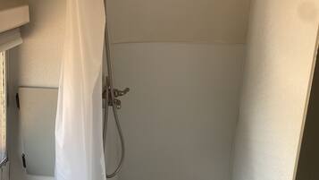 A small, compact shower area with a showerhead, a curtain, and a tiled floor.