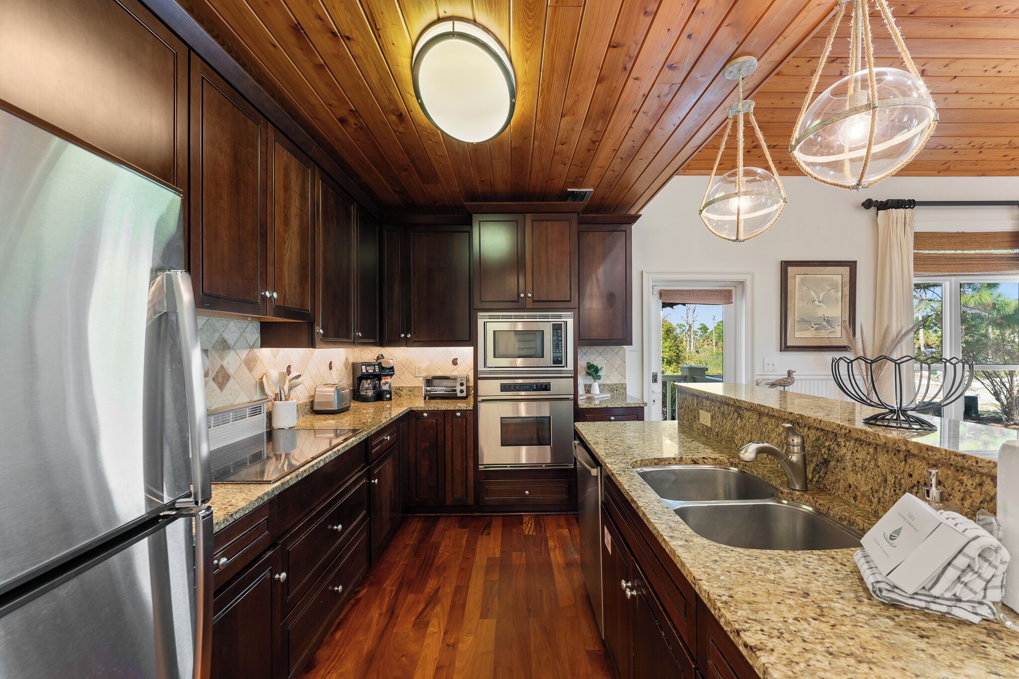 A modern kitchen with dark wood cabinets, stainless steel appliances, granite countertops, and pendant lighting.