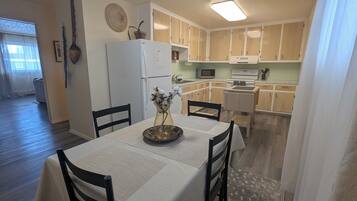 Un coin repas avec une table dressée pour deux personnes, un réfrigérateur et des meubles en bois en arrière-plan.