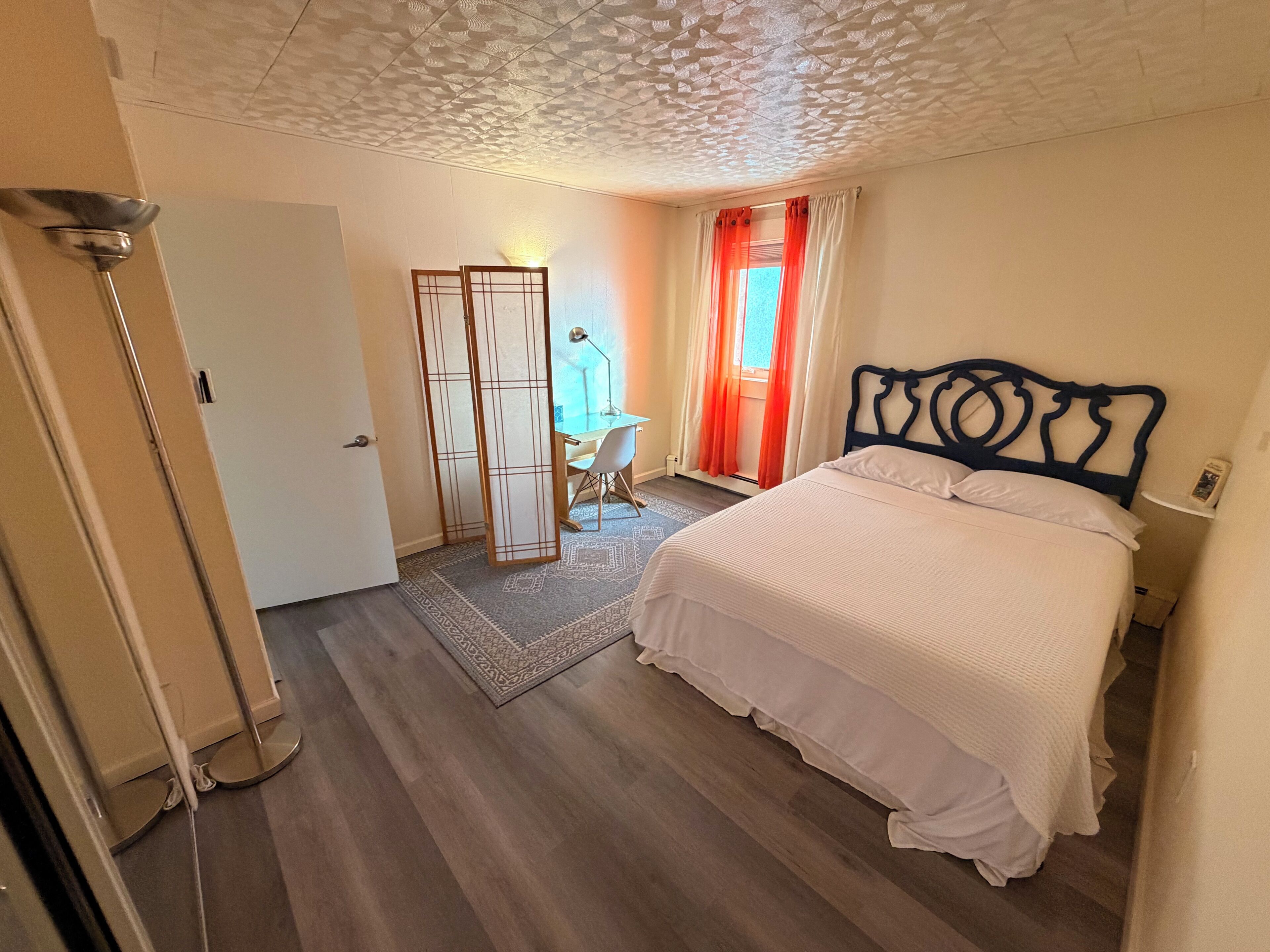 Une chambre à coucher comprenant un lit, un bureau, une chaise, une armoire et une lampe sur pied.