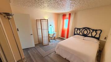 Une chambre à coucher comprenant un lit, un bureau, une chaise, une armoire et une lampe sur pied.