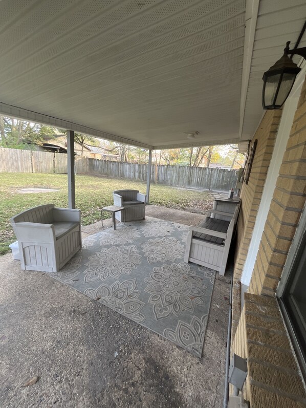 A covered patio area with a concrete floor, a patterned rug, and two white wooden chairs. - Springdale house (D'Iberville)