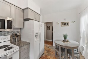 Enjoy meals in this kitchen with a stove, refrigerator, and microwave, accompanied by a dining area with a round table and two chairs.