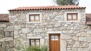 Un bâtiment en pierre avec un toit en tuiles, deux fenêtres à cadre en bois et une porte en bois.