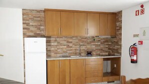 Une cuisine avec des meubles en bois, un réfrigérateur blanc, un évier et un extincteur fixé au mur.